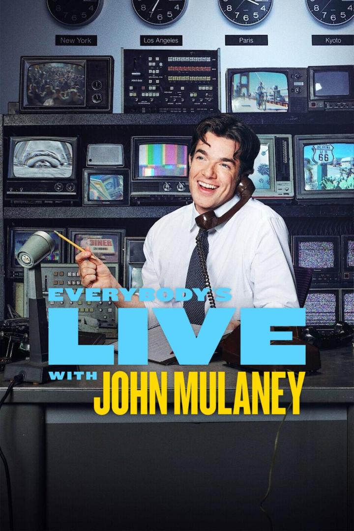 John Mulaney am Set von „Everybody's in LA“, umgeben von alten Fernsehern und Weltzeituhren.