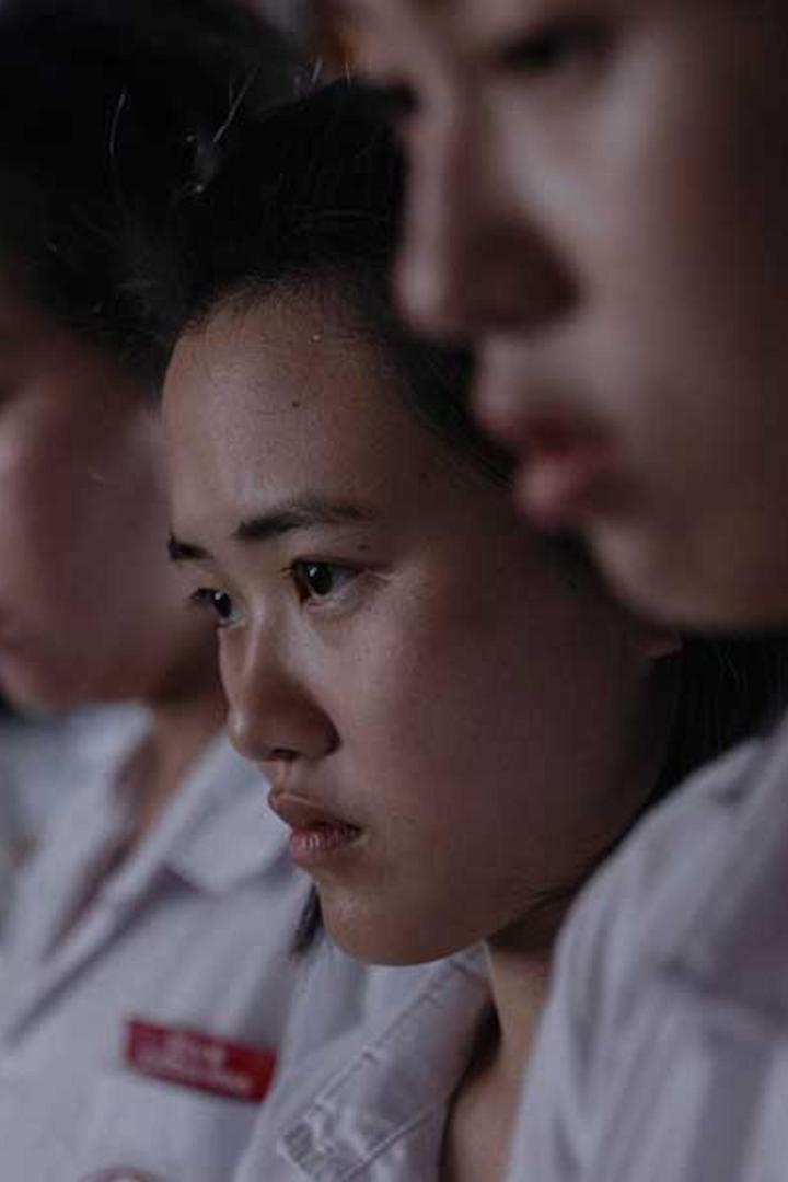 Eine junge Frau mit ernstem Blick in einem Klassenzimmer.