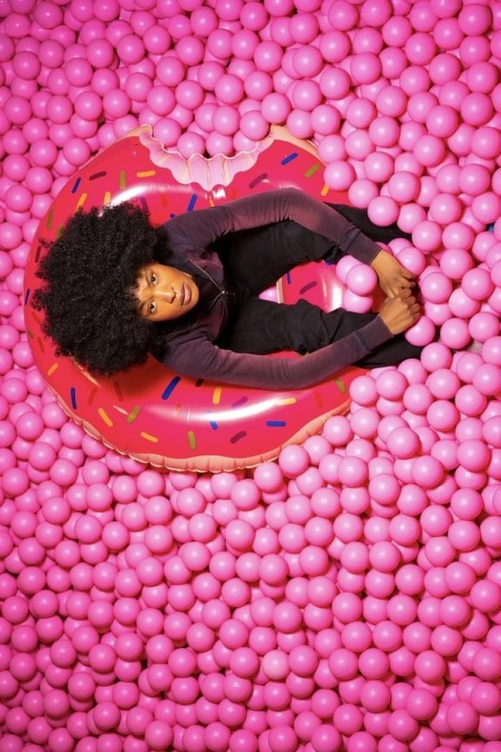 Eine Frau liegt auf einem Donut-förmigen Schwimmreifen in einem Becken voller pinkfarbener Bälle.
