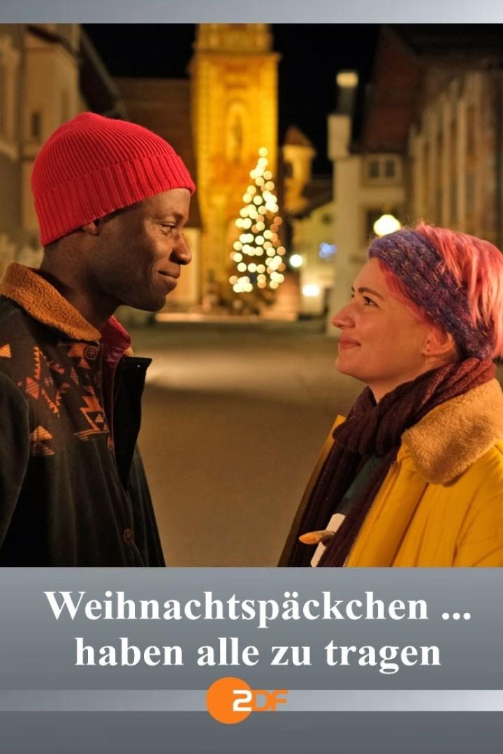 Ein Mann und eine Frau stehen sich vor einem Weihnachtsbaum an und lächeln sich an.