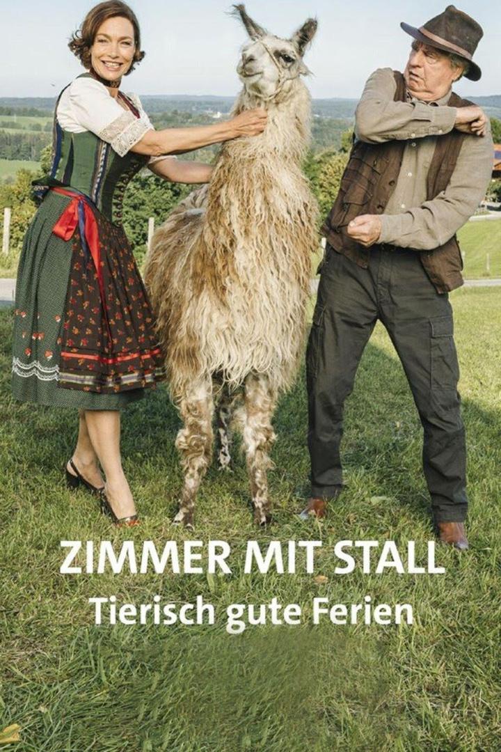 Eine Frau im Dirndl und ein Mann mit Hut umarmen ein Lama auf einer Wiese.