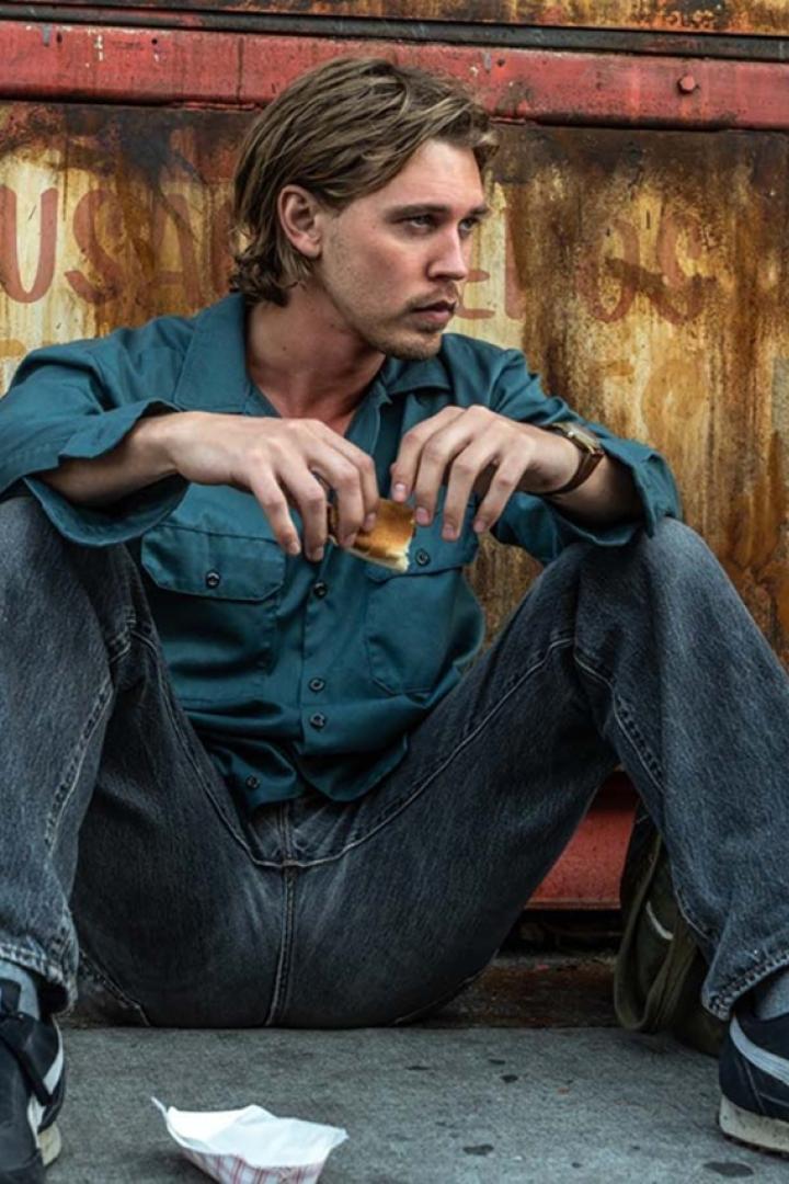 Austin Butler sitzt in "Caught Stealing" auf dem Boden vor einem herungergekommenen Lokal