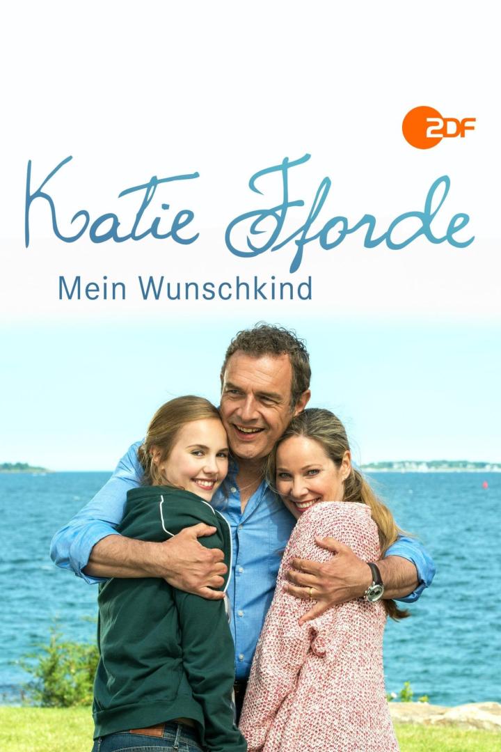 Das Filmplakat zu „Katie Fforde: Mein Wunschkind“ zeigt drei lächelnde Personen vor einer Küstenlandschaft.