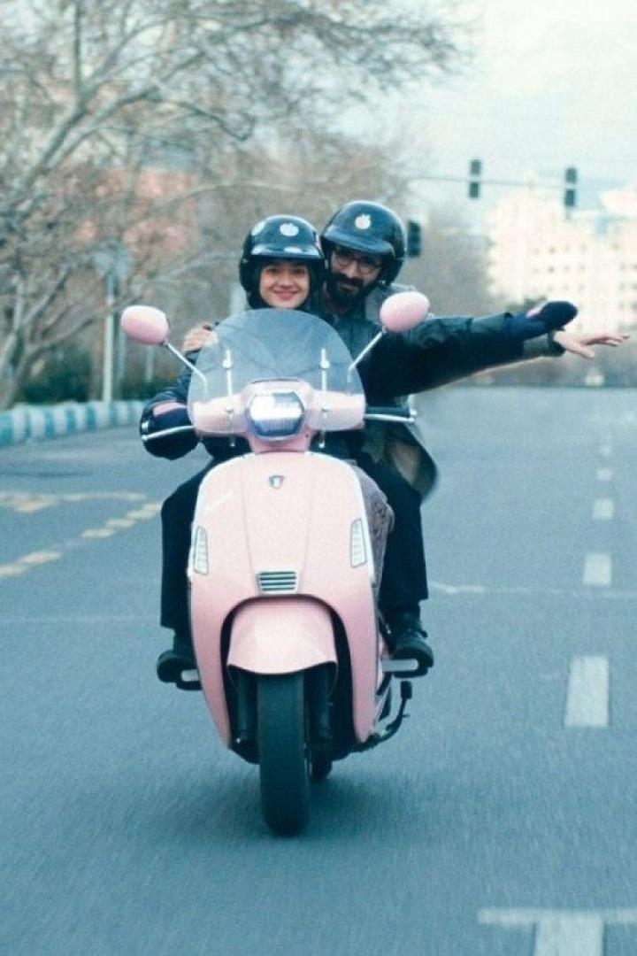 Ein Paar fährt mit einem rosa Motorroller auf einer Straße.