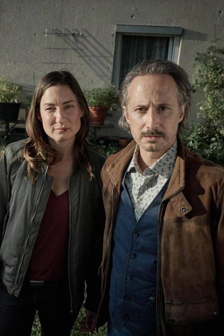 Eine Frau und ein Mann stehen vor einer Hauswand mit Pflanzenkübeln.