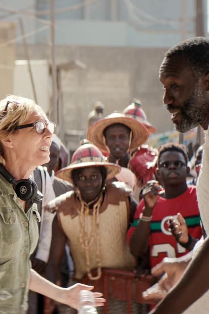 Eine Frau mit Kopfhörern spricht mit einer Gruppe von Menschen in traditioneller Kleidung.