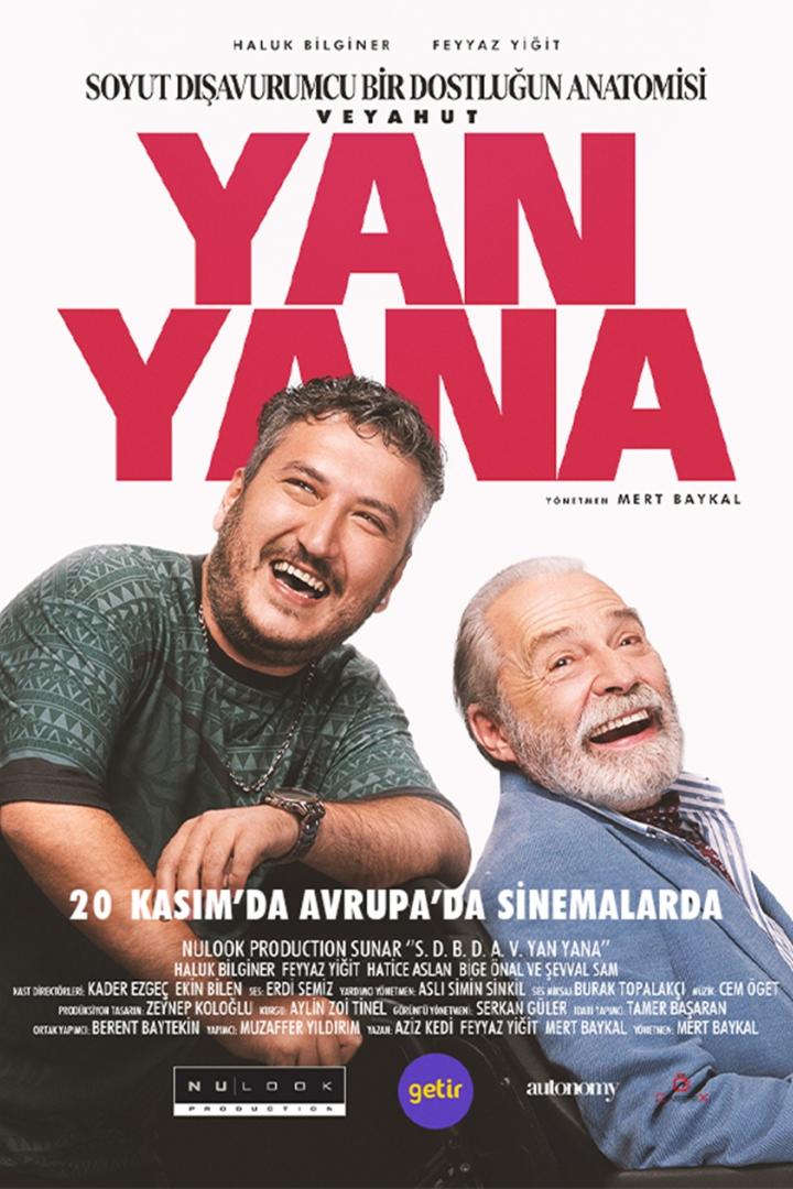 Jüngerer Mann lehnt sich auf die Rückenlehne eines Rollstuhles, in dem ein älterer Mann sitzt