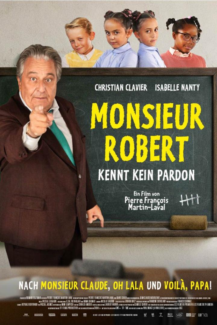 Christian Clavier steht vor einer Schultafel, die den Fimtitel trägt und zeigt mit dem Finger auf uns