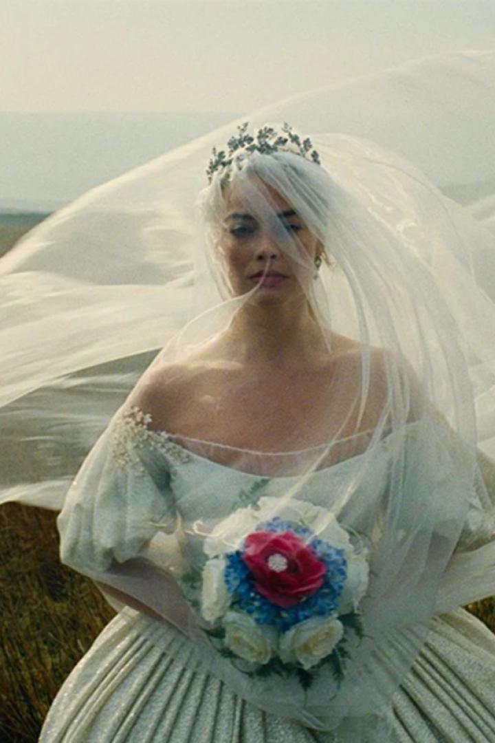 Margot Robbie in Brautkleid mit weißem wehendem Schleier auf der Heide