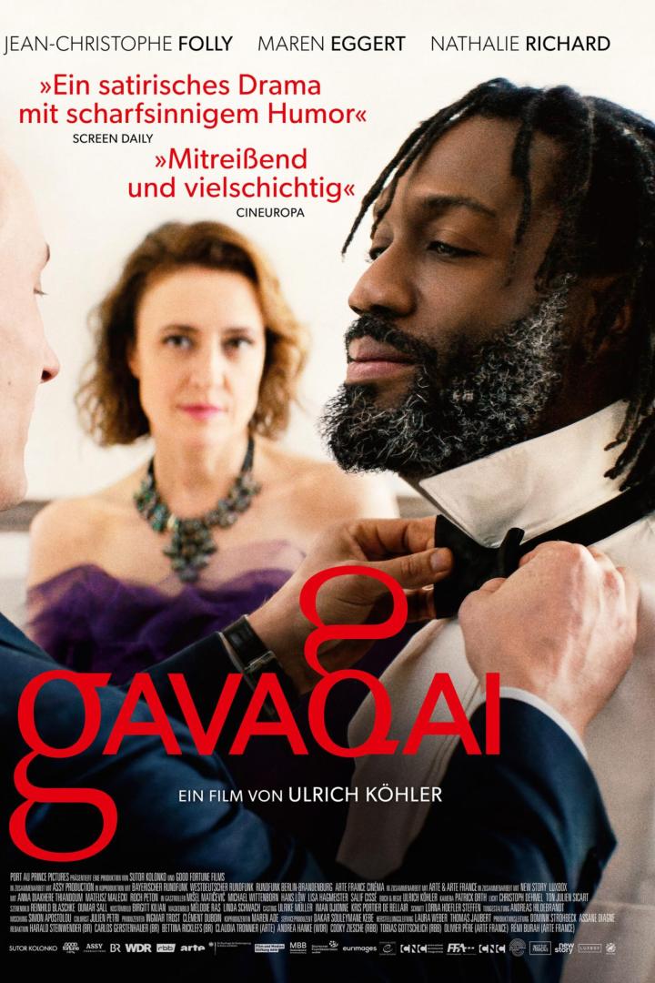 Ein Mann befestigt einem anderen Mann eine Fliege am Hemd, im Hintergrund steht eine Frau