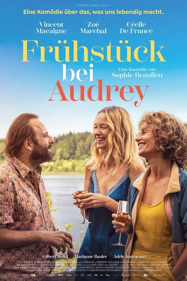 Filmplakat für „Frühstück bei Audrey“ mit Vincent Macaigne, Zoé Marchal und Cécile De France, die lachend mit Weingläsern vor einem See stehen.
