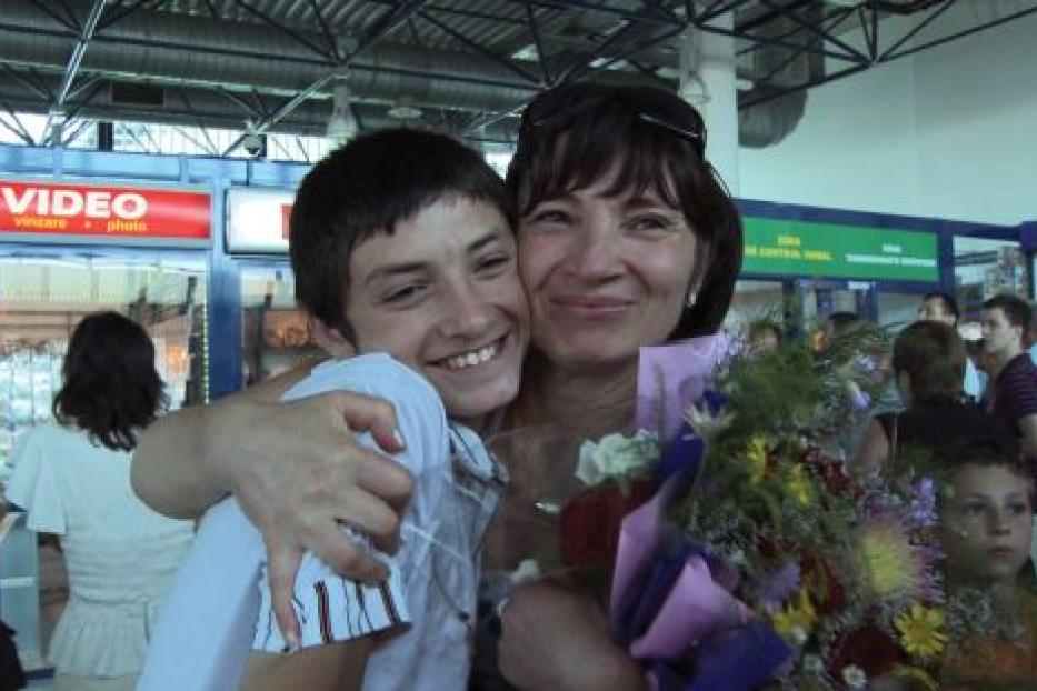 Eine Frau umarmt einen jungen Mann und hält einen Blumenstrauß in einem belebten Terminal.