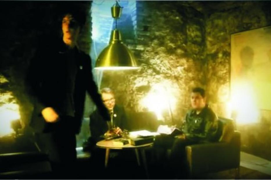 Drei Personen in einem spärlich beleuchteten Raum mit Steinhintergrund.