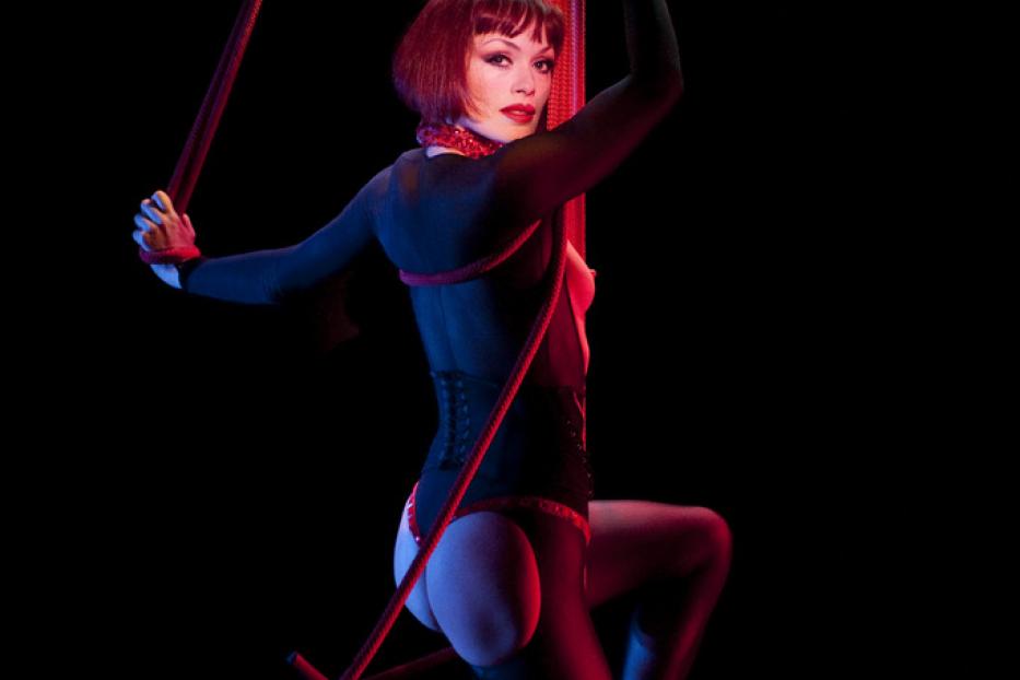 Eine Frau mit roten Haaren performt eine akrobatische Übung an roten Seilen.