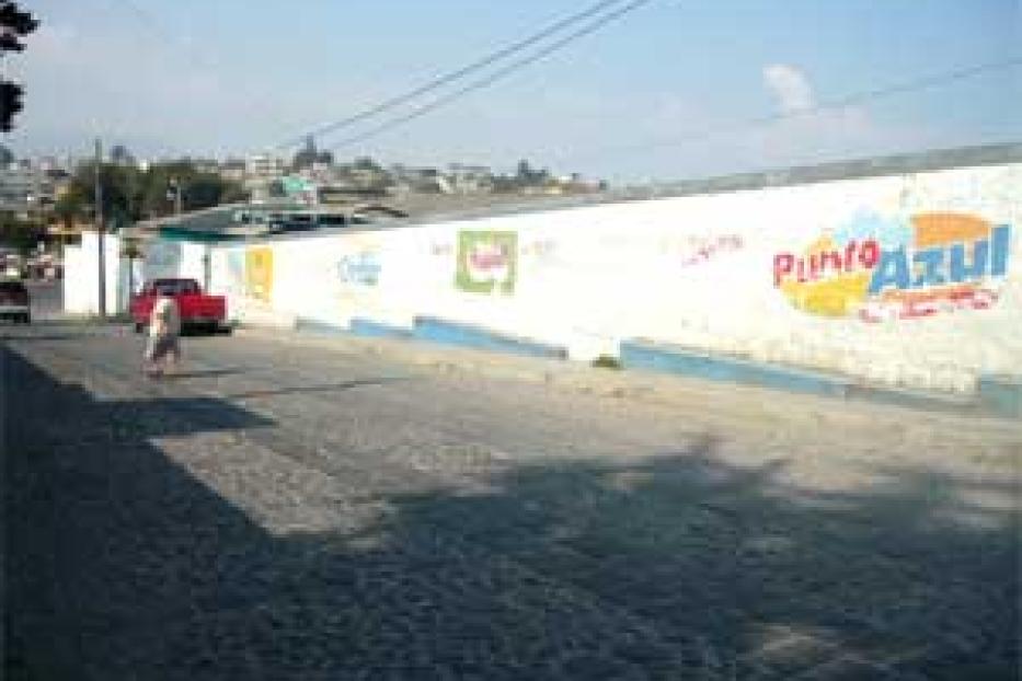 Eine Person geht an einer langen, weißen Mauer mit Werbeaufschriften vorbei.