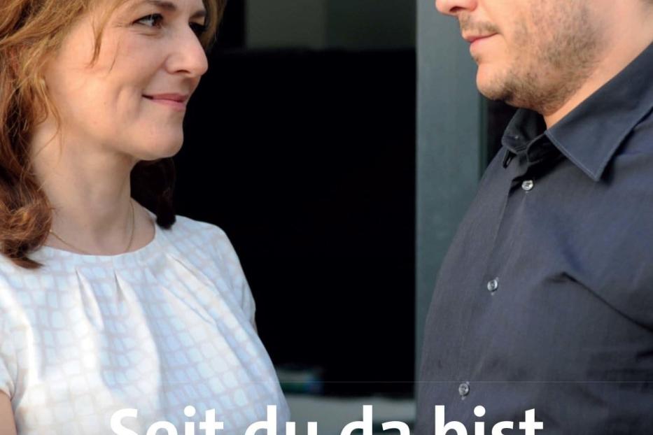 Eine Frau und ein Mann schauen sich an; Filmposter „Seit du da bist“.