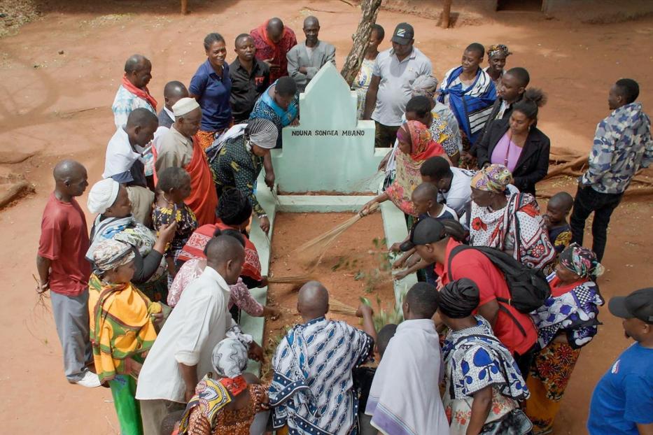 Eine Gruppe von Menschen versammelt sich um ein Grab mit der Aufschrift „Nduna Songea Mbano“.