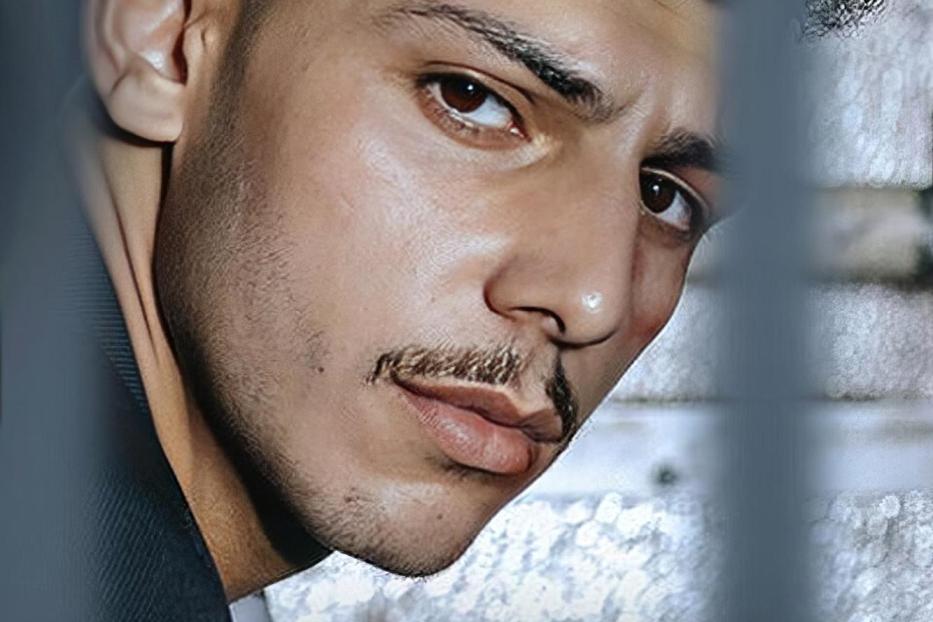 Ein Mann mit Schnurrbart blickt hinter Gittern hervor; im Vordergrund steht das Wort „ASBEST“.