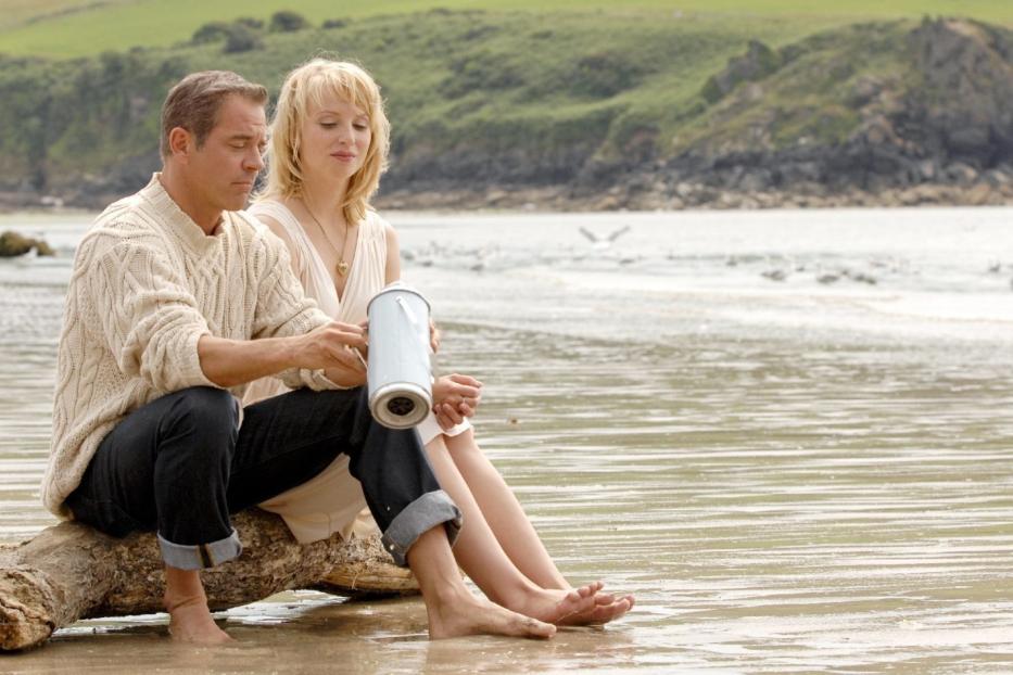 Ein Paar sitzt barfuß am Strand und betrachtet eine Urne.