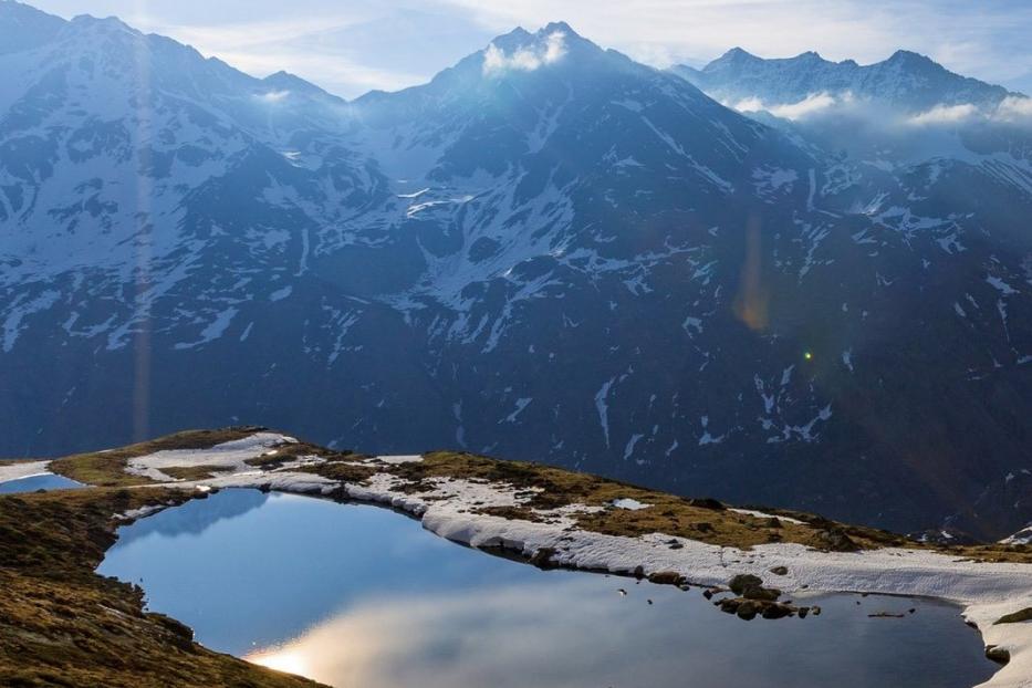Ein Bergsee in den Alpen spiegelt die umliegenden schneebedeckten Gipfel wider.