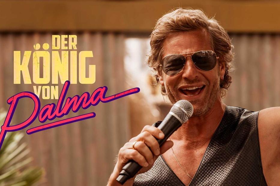 Ein Mann mit Sonnenbrille singt in ein Mikrofon, im Hintergrund der Schriftzug „Der König von Palma“.