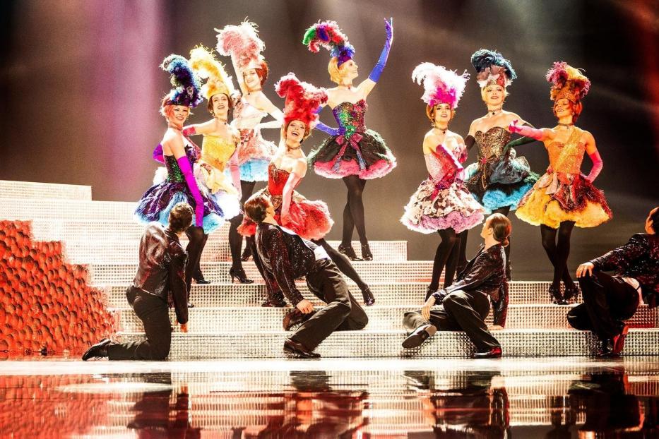 Eine Gruppe von Tänzerinnen in farbenprächtigen Kostümen und Kopfbedeckungen auf einer Bühne.