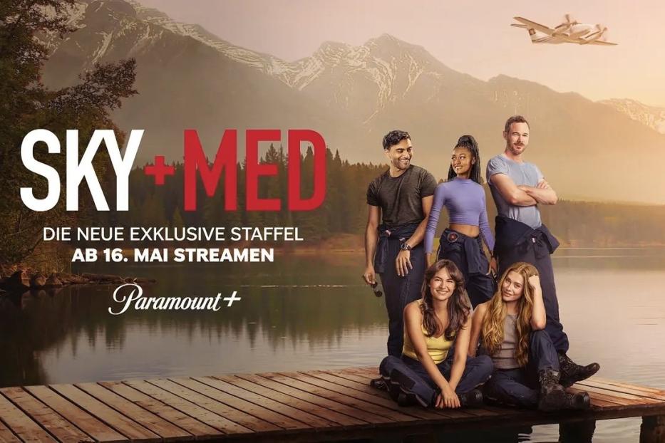 Die Besetzung von „SkyMed“ posiert vor einem Bergsee mit einem Wasserflugzeug in der Luft.