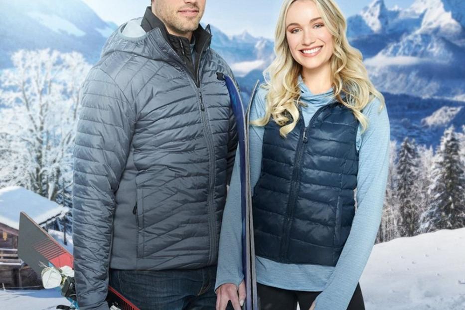 Ein Mann und eine Frau mit Skiern vor einer verschneiten Bergkulisse für „Liebe auf der Piste“.