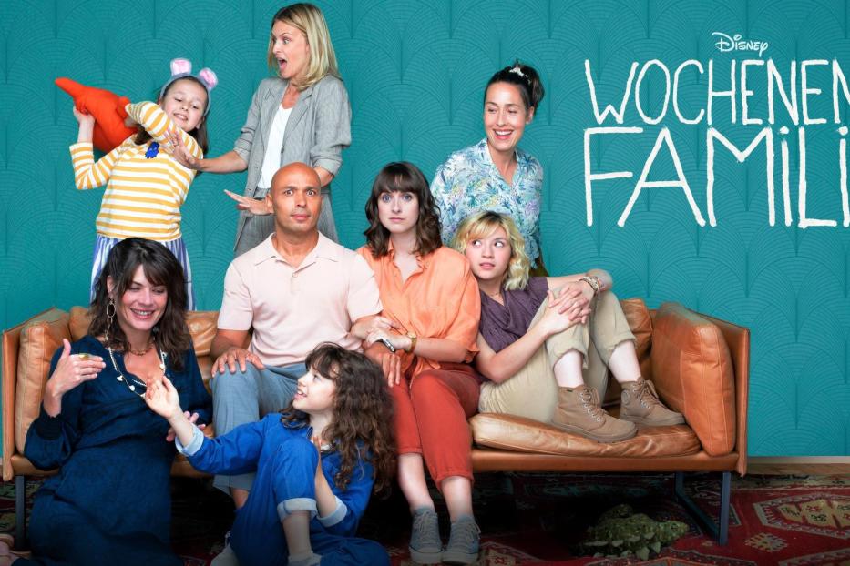 Das Gruppenbild der Besetzung der Disney+ Serie „Wochenend Familie“ vor einem türkisfarbenen Hintergrund.