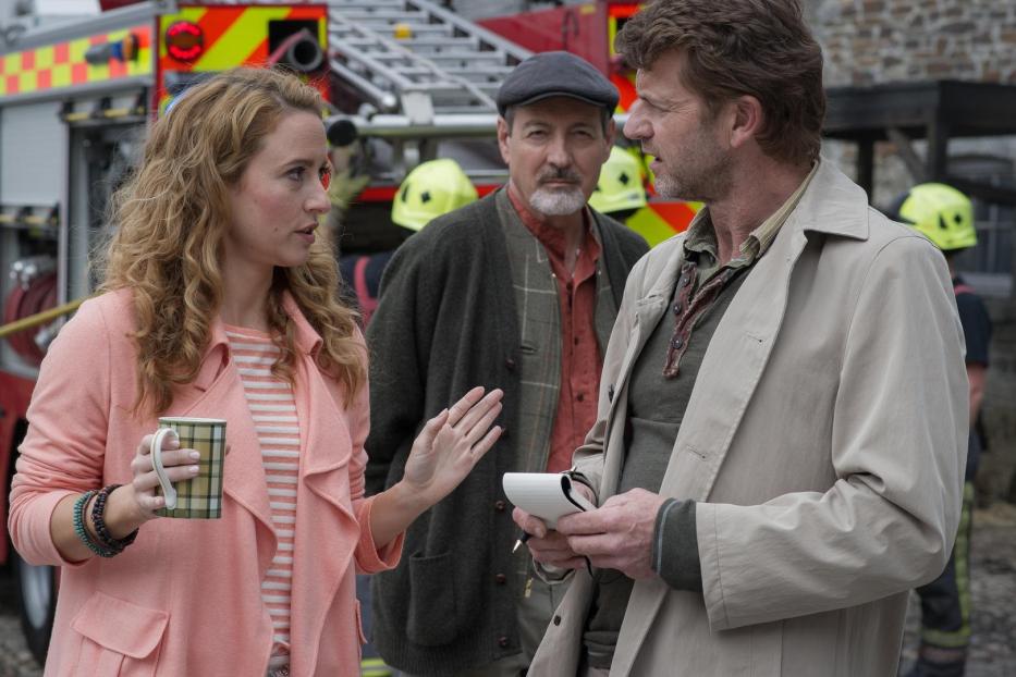 Eine Frau mit einer Tasse spricht mit einem Mann vor einem Feuerwehrauto.