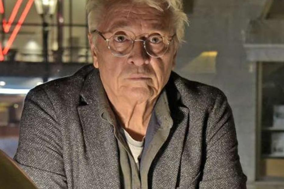 Ein Mann sitzt an einem Tisch mit einem Buch, im Hintergrund der Titel „Spätwerk“.