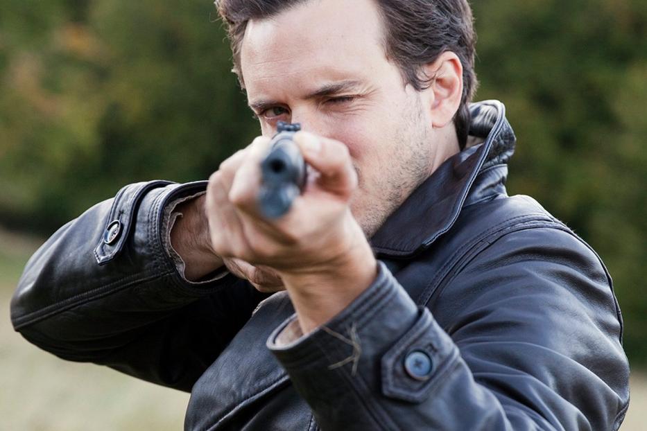 Ein Mann im Ledermantel zielt mit einem Gewehr.