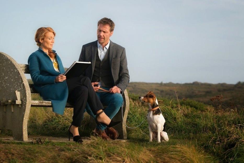 Ein Paar sitzt mit einem Hund auf einer Bank in der Natur.