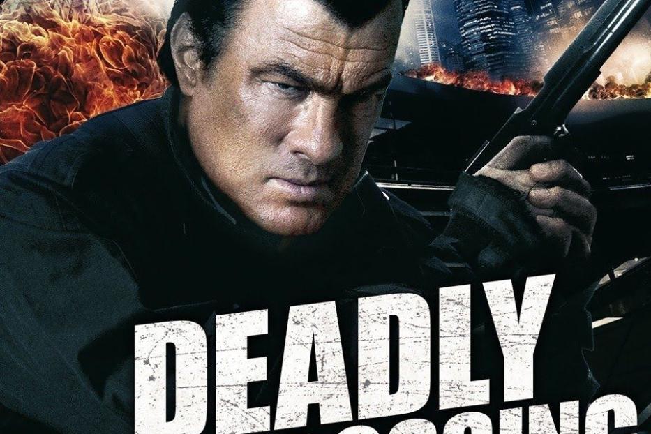 Das Filmplakat für „Deadly Crossing – Tödliche Grenzen“ zeigt Steven Seagal mit einer Waffe vor einer zerstörten Stadt.