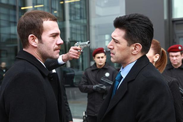 Ein Mann bedroht einen anderen Mann mit einer Pistole vor einem Gebäude.