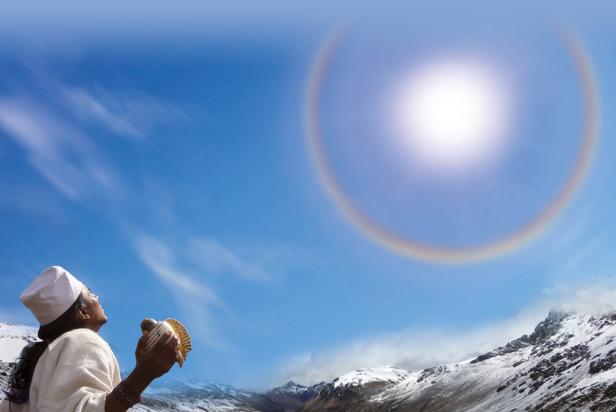 Eine Frau hält eine Muschel in den Händen und blickt auf einen Halo um die Sonne vor einer Bergkulisse.