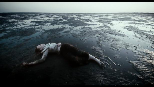 Eine Frau liegt erschöpft im Watt.