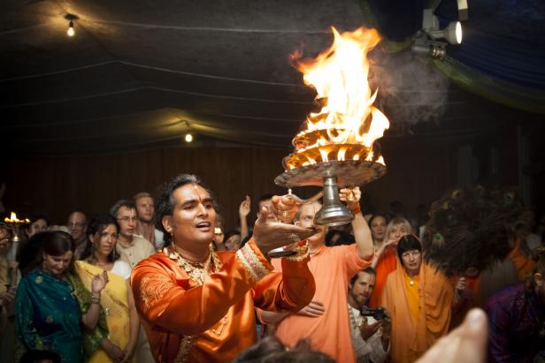 Ein Mann in orangefarbener Kleidung hält eine Schale mit brennenden Flammen hoch.