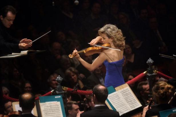 Eine Geigerin spielt vor einem Orchester und Publikum.