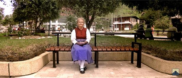 Eine ältere Frau sitzt auf einer Bank in einem Park.