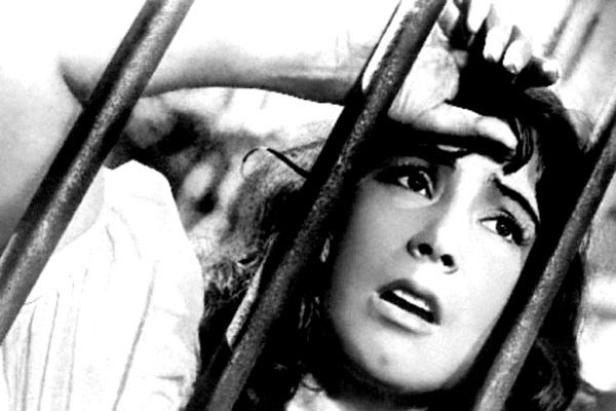 Eine verängstigte Frau blickt hinter Gittern hervor.