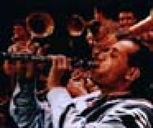 Ein Mann spielt Klarinette, umgeben von anderen Musikern mit Blasinstrumenten.