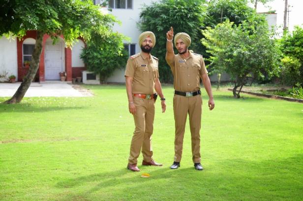 Zwei Sikh-Polizisten stehen auf einem Rasen, einer zeigt nach oben.