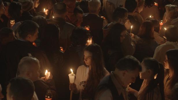 Eine Menschenmenge hält brennende Kerzen in der Dunkelheit.