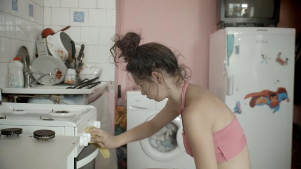 Eine junge Frau putzt den Herd in einer Küche.