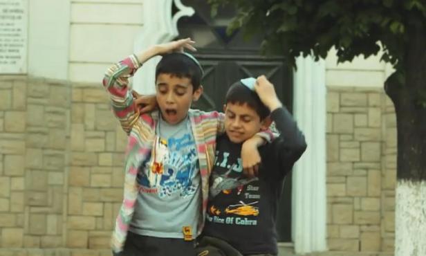 Zwei jüdische Jungen mit Kippa umarmen sich vor einem Gebäude.