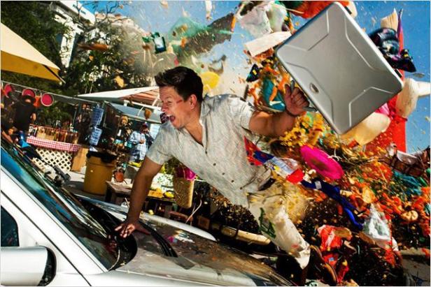 Mark Wahlberg weicht auf einem Markt einer Explosion aus, einen Koffer hochhaltend.