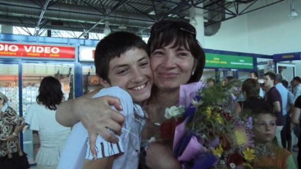 Eine Frau umarmt einen jungen Mann und hält einen Blumenstrauß in einem belebten Terminal.