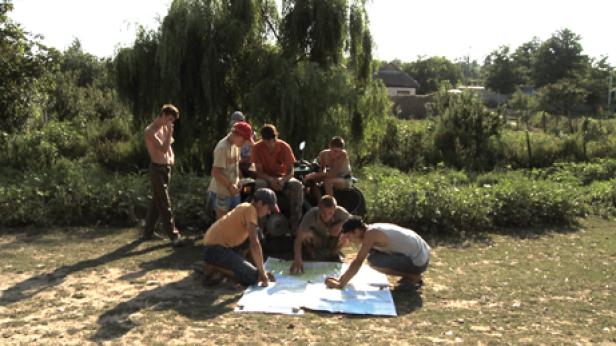 Eine Gruppe junger Männer studiert eine Karte neben einem Quad im Grünen.