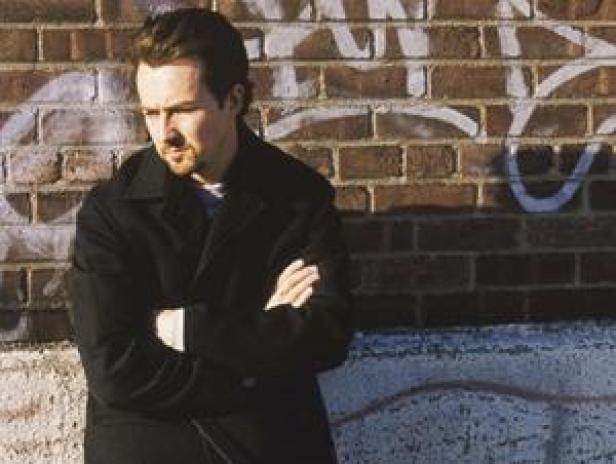 Ein Mann mit verschränkten Armen steht vor einer Backsteinmauer.